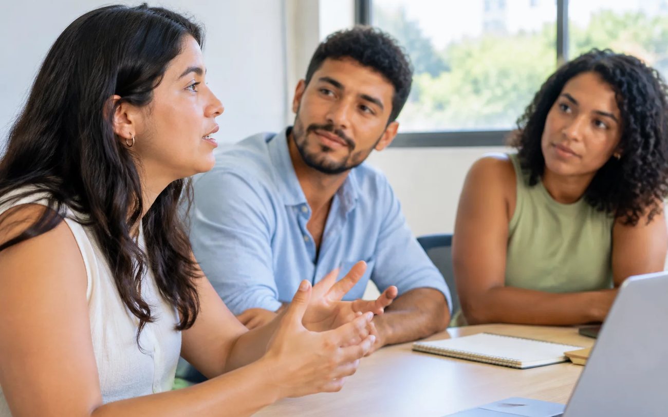 Roda de conversa numa sala clara, com uma pessoa expondo o ponto e duas escutando